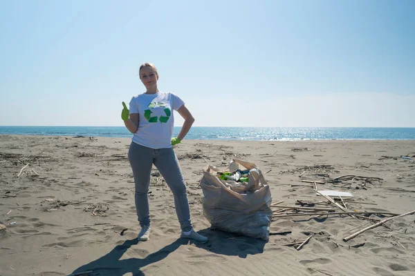 woman picks up trash from the beach in trash bags