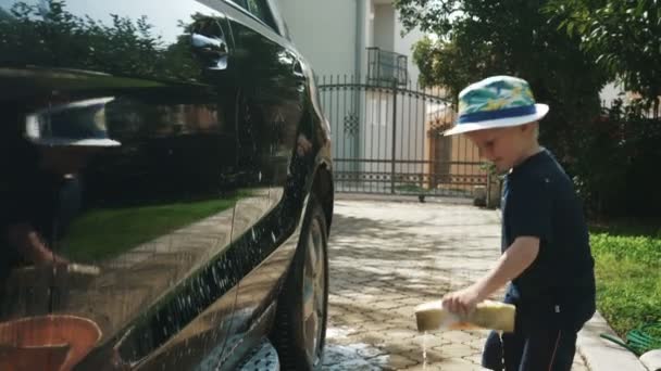 Мальчик в шляпе моет машину с мылом и губкой — стоковое видео