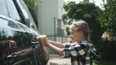 Sekiz yaşında bir kız, sabun ve süngerle araba yıkıyor.