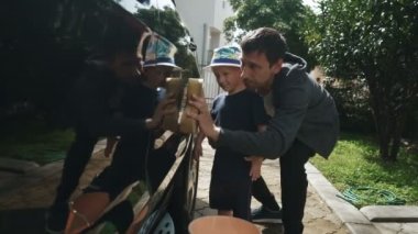 Baba oğluna araba yıkamayı öğretir.