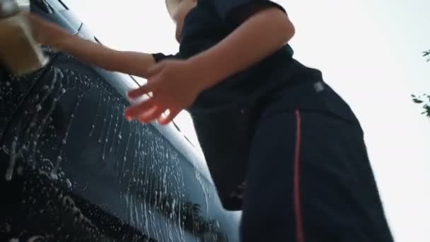 Niño en un sombrero lava un coche con jabón y una esponja — Vídeos de Stock