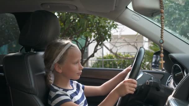 Niña de ocho años sentada al volante de un coche — Vídeos de Stock