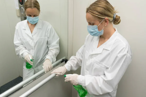 Vrouw die natte doekjes en alcohol ontsmettingsspray gebruikt om de reling in de lift schoon te maken. Desinfectie, reinheid en gezondheidszorg, Anti Coronavirus COVID-19 — Stockfoto