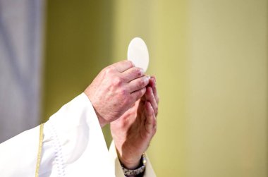 during the celebration of the Mass the hands of the priest, like the hands of Pope Francis, consecrate the host which becomes the body of Christ clipart