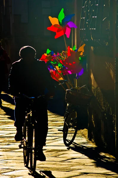 senior on bicycle with pinwheel of all colors in sunset light