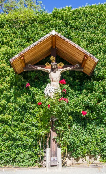 私たちのために十字架につけられたイエス キリストの彫刻となった山の木緑の植物や赤いバラの中に住む人々の自発的な宗教 — ストック写真