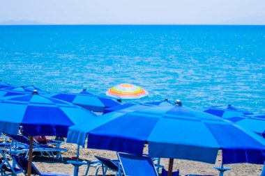 Arka planda mavi deniz olan mavi şemsiyeler. Yazın resim gibi üç farklı sembolü.