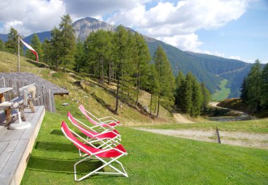 Kırmızı şezlonglar dinlenmek için ve yüksek dağlara hayran yeşil çayırlar ve yemyeşil ormanlar ve mavi gökyüzünün altında keskin kayalar