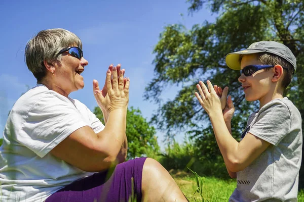 Grootmoeder en kleinzoon spelen met hun handen op het groene gazon . — Stockfoto