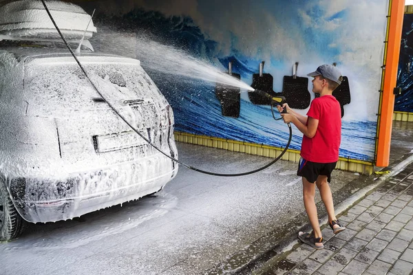Adolescente ayuda a lavar el coche en el lavado de coches con espuma  . — Foto de Stock