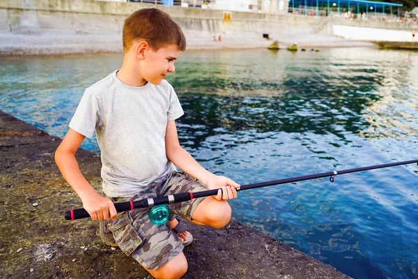 A boy with a fishing rod catches fish from the pier in the sea . — Stock Photo, Image