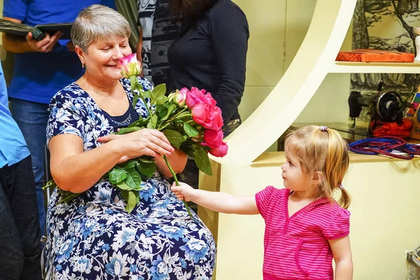 Das Mädchen gratuliert ihrer Großmutter und schenkt Blumen . — Stockfoto