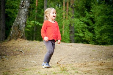 3 yaşında neşeli küçük bir kız ormanın ortasında oyun oynuyor. .