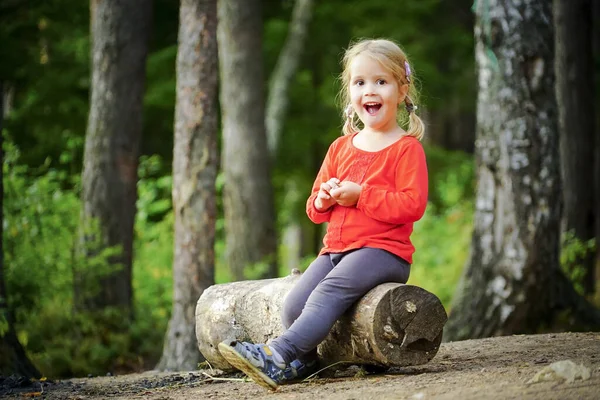 Una piccola ragazza allegra di 3 anni è seduta su un tronco nella foresta . — Foto Stock