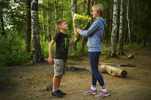 Zoon geeft bloemen aan zijn moeder in de natuur op het meer. — Stockfoto