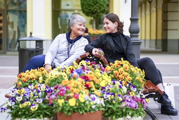 Młoda Dziewczyna Rozmawia Starszą Kobietą Siedzącą Ławce Wśród Kwiatów — Zdjęcie stockowe
