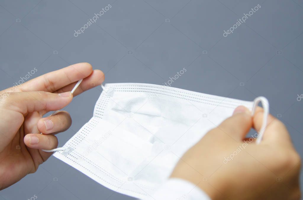 White surgical mask  in hand on grey background.