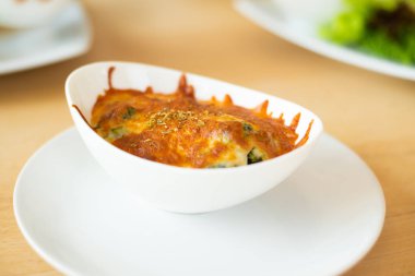 Ahşap masada beyaz kasede peynirli fırınlanmış ıspanak..