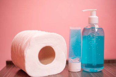 Alkol jeli şişesini ve tuvalet kağıdını koruma altına alınmış Corona ya da pembe pastel arka planda Covid-19 virüsü ile kapatın..