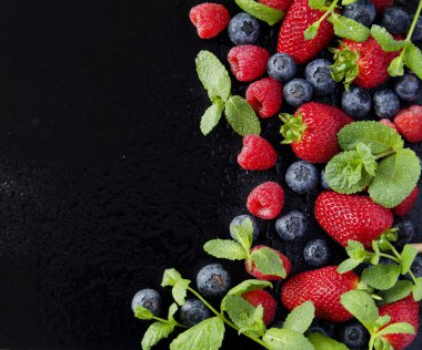 taze çilek, ahududu ve siyah bir arka plan üzerinde yaban mersini