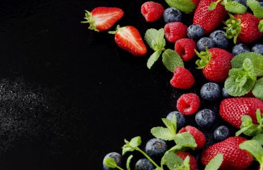 taze çilek, ahududu ve siyah bir arka plan üzerinde yaban mersini