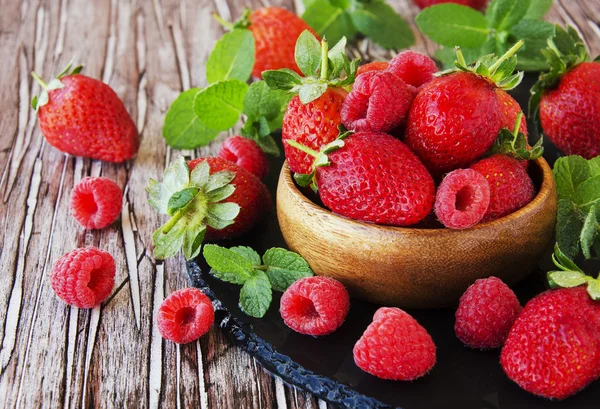 Ripe red raspberries and strawberries in wooden bowl, selective focus — Stock Photo, Image