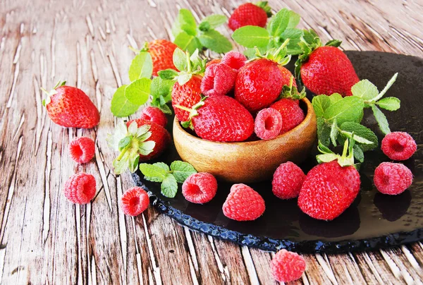 Ripe red raspberries and strawberries in wooden bowl, selective focus — Stock Photo, Image