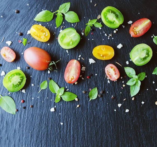 Mitades rojas y negras de tomates con hojas verdes albahaca —  Fotos de Stock