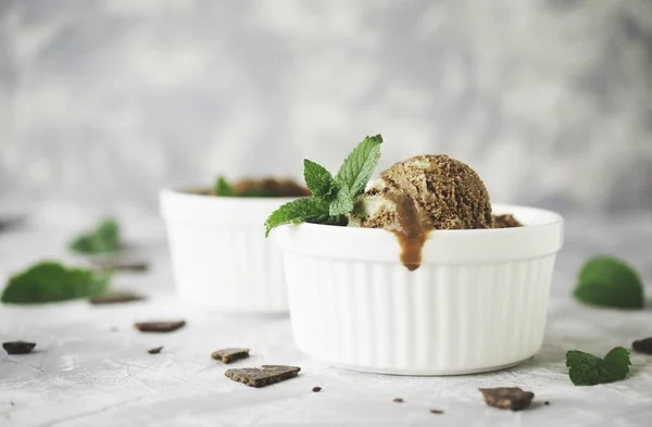 chocolate mint ice cream in white bowls with pieces of chocolate and mint leaves on a marble table