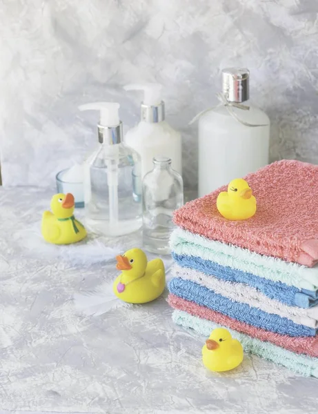 stack of towels with yellow rubber bath ducks on white marble background, space for text, selective focus