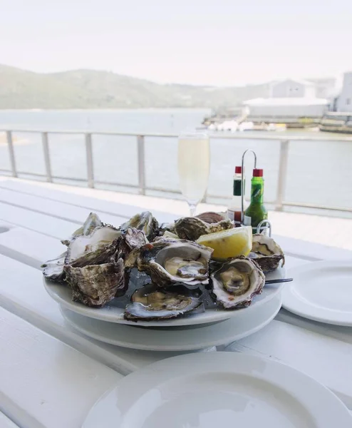a plate of fresh open oysters and a glass of champagne on a white table with a view of the ocean, selective focus
