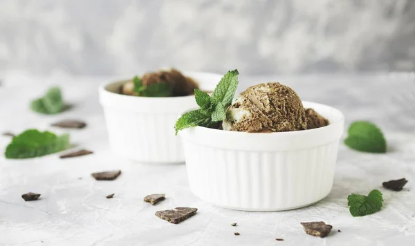 chocolate mint ice cream in white bowls with pieces of chocolate and mint leaves on a marble table