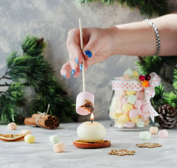 Pane tostato un marshmallow sopra una candela durante Natale e Anno nuovo su un tavolo bianco di legno, messa a fuoco selettiva — Foto Stock