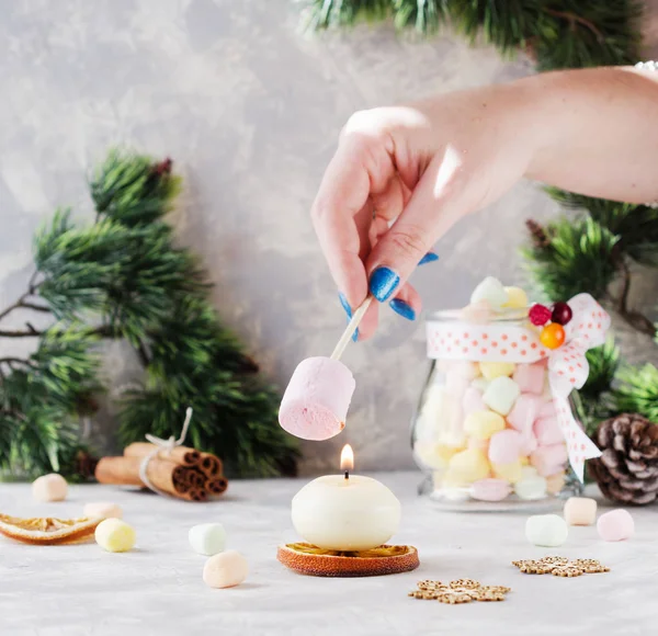 Pane tostato un marshmallow sopra una candela durante Natale e Anno nuovo su un tavolo bianco di legno, messa a fuoco selettiva — Foto Stock