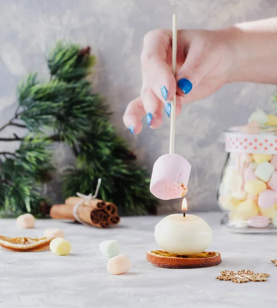 Pane tostato un marshmallow sopra una candela durante Natale e Anno nuovo su un tavolo bianco di legno, messa a fuoco selettiva — Foto Stock