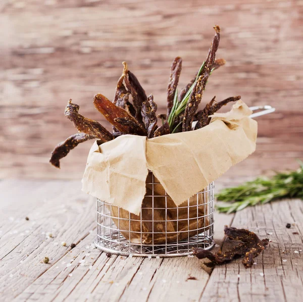 Jerked meat, cow, deer, wild beast or biltong in kraft paper bowls on a rustic table, selective focus — Stock Photo, Image