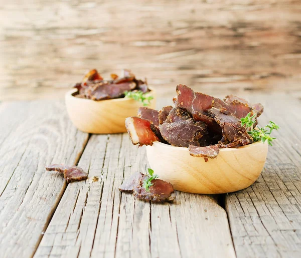 Jerked meat, cow, deer, wild beast or biltong in wooden bowls on a rustic table, selective focus — Stock Photo, Image