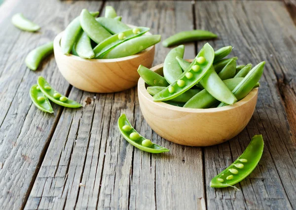 Green peas in a wooden bowl on a rustic table, selective focus — Stock Photo, Image