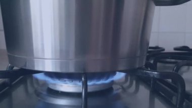 Mavi gaz alevi yanan bir sobanın üzerindeki paslanmaz çelik tavayı ısıtıyor. Video soğuk mavi tonlarda yapılır.