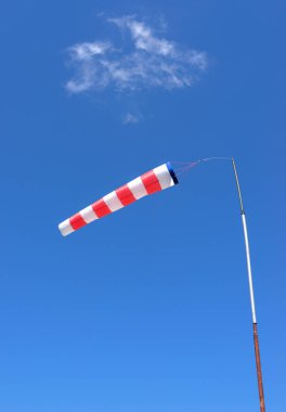 Red and white windsock made of fabric hangs almost horizontally on a pole against a blue sky with a slight cloud clipart