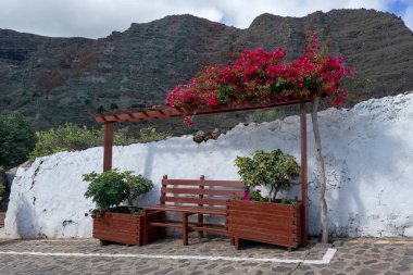 Idyllic, beyaz bir duvarın önündeki eğimli bir yolda, dağlara ahşap bir bank dikti.