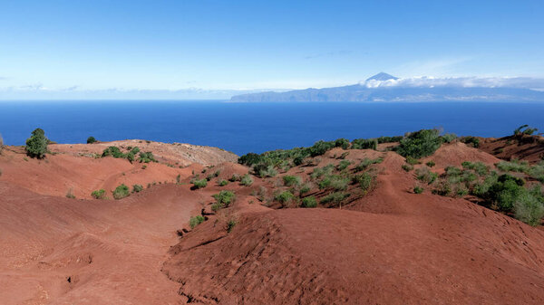 Ла-Гомера, Канарские острова - эрозионный ландшафт с красной почвой на северном побережье над Агуло с видом на Тенерифе
