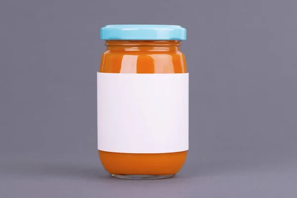 Orangefarbenes Glas für Babynahrungsbank auf grauem Hintergrund. Bio-Babynahrungspüree. Mock-up ohne Vorlage Design-Etikett. — Stockfoto