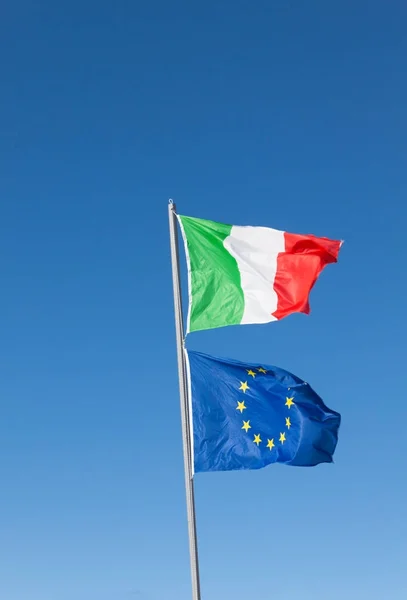 Flags of Italy and Europe waving in the wind on blue sky background