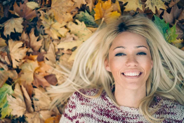 Retrato de una mujer rubia acostada en hojas de otoño — Foto de Stock