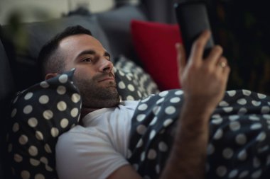 Genç bağımlısı adam uyanık gece yatakta smartphone kullanarak 