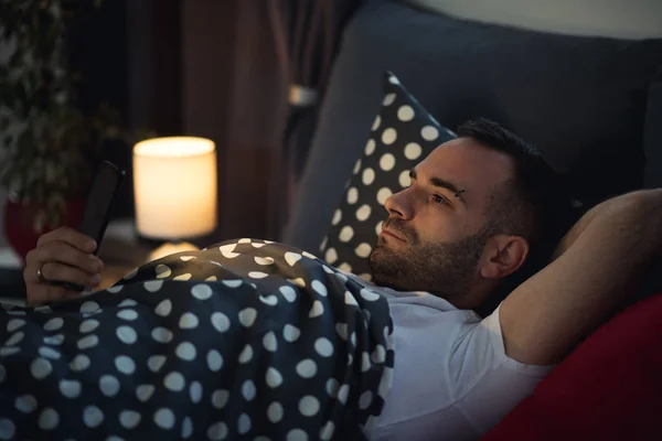 Young addict man awake in bed using smartphone — Stock Photo, Image