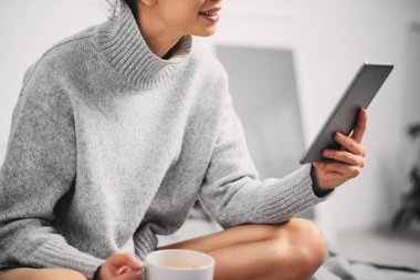 Kız sabah yatağın üstüne oturan ve haber okumak için tablet kullanma 