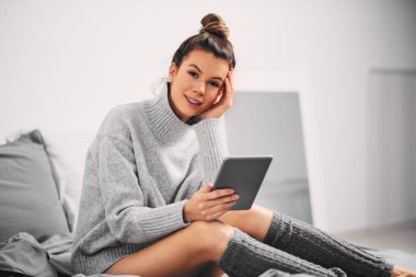 Sabahleyin yatakta otururken tablet kullanan kadın.