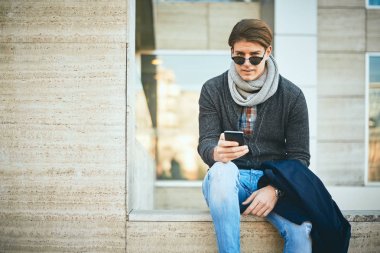 Açık ve kullanma akıllı telefon oturan genç adam.